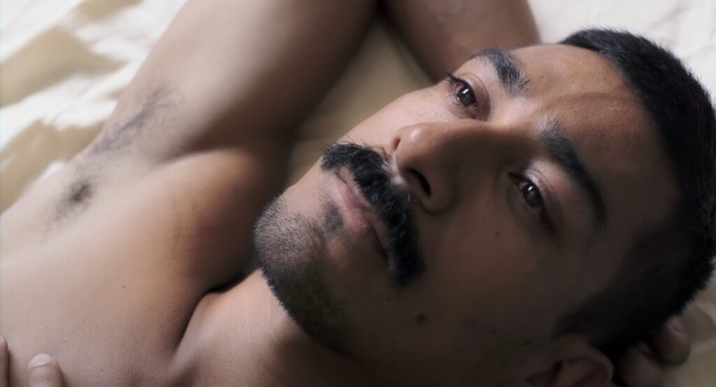 Still from the film Pornomelancholia by Manuel Abramovich: Lalo Santos, the main character of the film, is lying on the bed and looking at the ceiling with an emotional expression