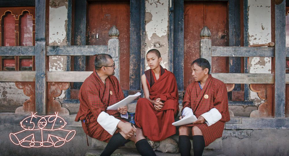 Z&aacute;ber z filmu Agent of Happiness: traja muži v budhistickom oblečen&iacute; sedia na schodoch pred budovou
